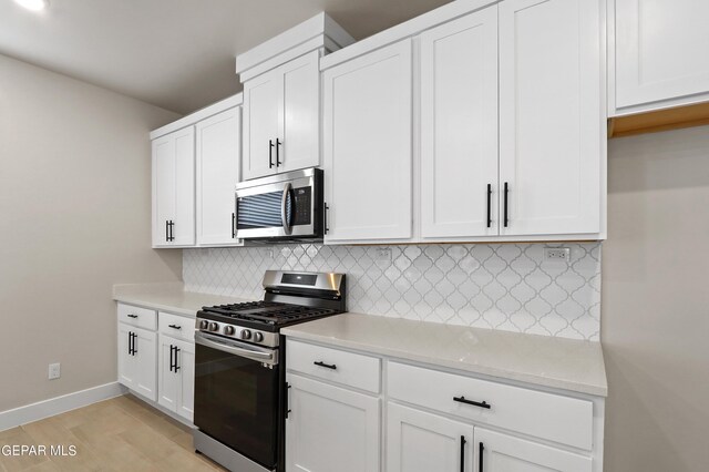 kitchen featuring backsplash, white cabinetry, stainless steel appliances, light stone countertops, and light hardwood / wood-style floors