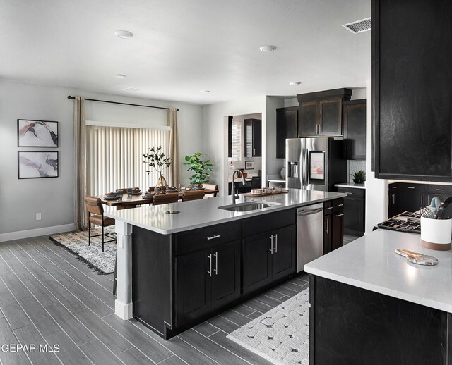 kitchen with a kitchen island with sink, sink, stainless steel appliances, and dark hardwood / wood-style flooring