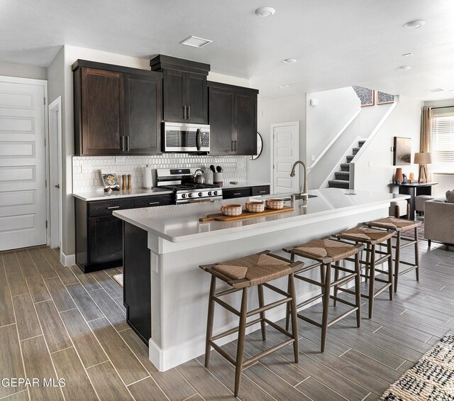 kitchen with a center island with sink, appliances with stainless steel finishes, a kitchen breakfast bar, dark hardwood / wood-style flooring, and decorative backsplash