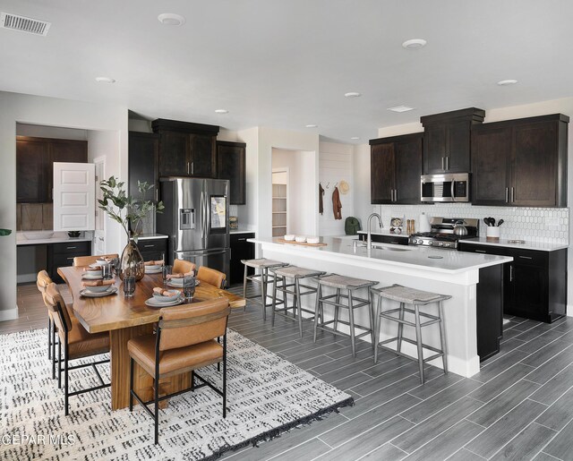 kitchen with appliances with stainless steel finishes, backsplash, a kitchen island with sink, hardwood / wood-style floors, and sink