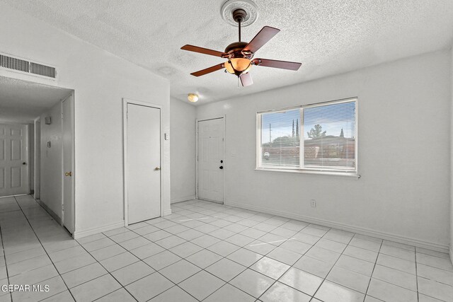 empty room featuring a textured ceiling, light tile patterned floors, and ceiling fan