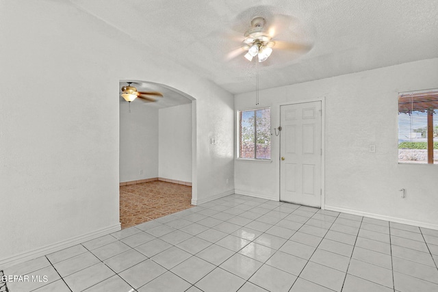 spare room featuring a textured ceiling, light tile patterned flooring, ceiling fan, and a wealth of natural light