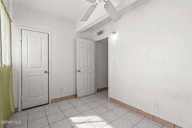 tiled empty room with ceiling fan and a textured ceiling