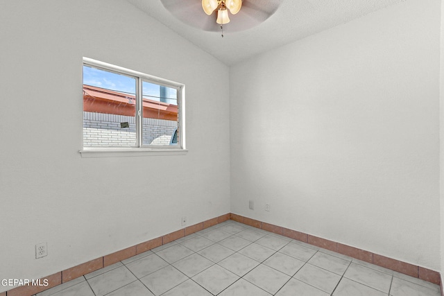 empty room featuring vaulted ceiling, ceiling fan, light tile patterned flooring, and a textured ceiling