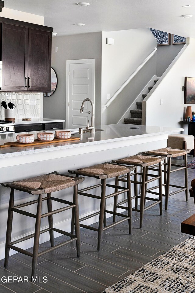 kitchen with dark brown cabinetry, backsplash, a breakfast bar area, and sink