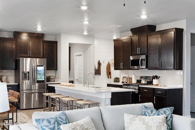 kitchen featuring appliances with stainless steel finishes, tasteful backsplash, a breakfast bar, dark brown cabinetry, and a kitchen island with sink