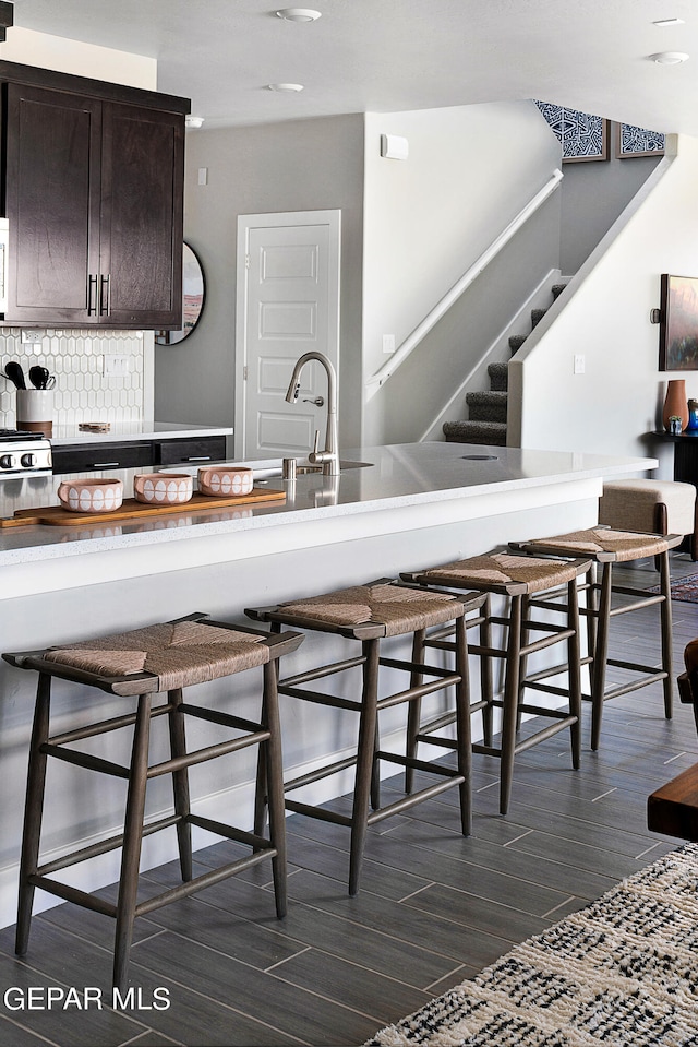 kitchen featuring decorative backsplash, sink, dark brown cabinetry, and a breakfast bar area