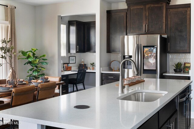 kitchen with decorative backsplash, light stone countertops, dark brown cabinetry, stainless steel refrigerator with ice dispenser, and sink