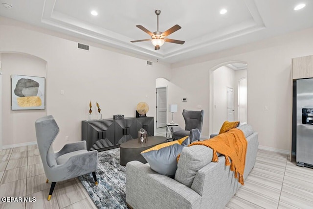 tiled living room with a raised ceiling and ceiling fan