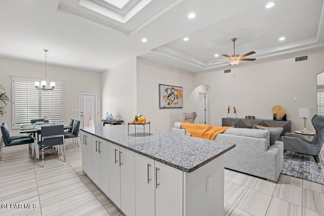 kitchen with ceiling fan with notable chandelier, white cabinets, a raised ceiling, and hanging light fixtures