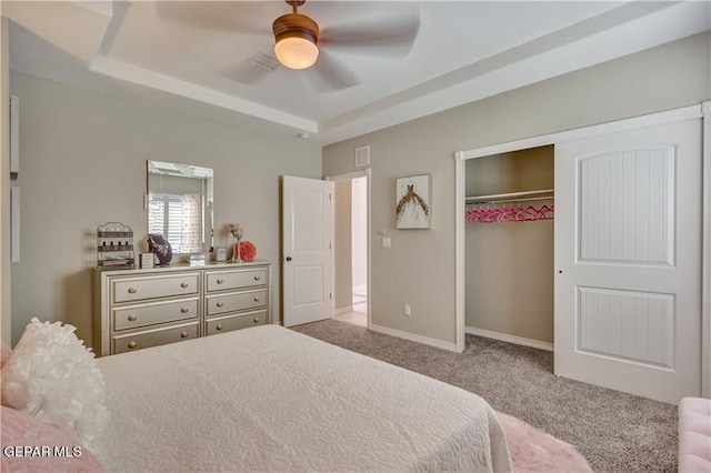 carpeted bedroom with a tray ceiling, ceiling fan, and a closet