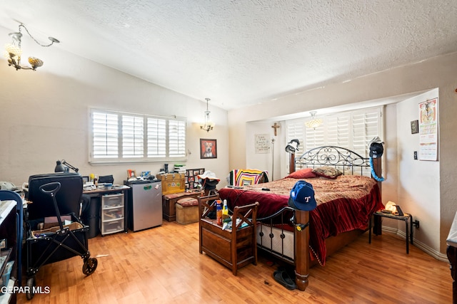 bedroom featuring vaulted ceiling, a textured ceiling, stainless steel fridge, and light hardwood / wood-style floors