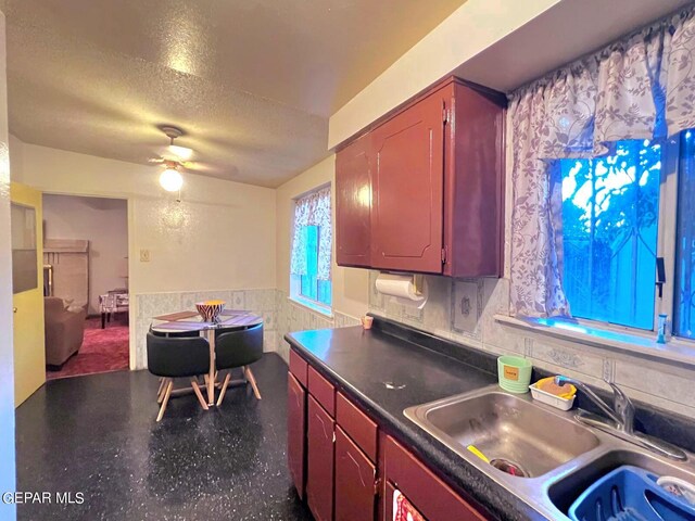 kitchen with ceiling fan, a textured ceiling, tile walls, and sink