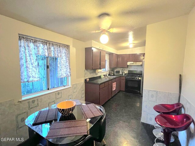 kitchen featuring tile walls, a textured ceiling, ceiling fan, black gas range, and sink