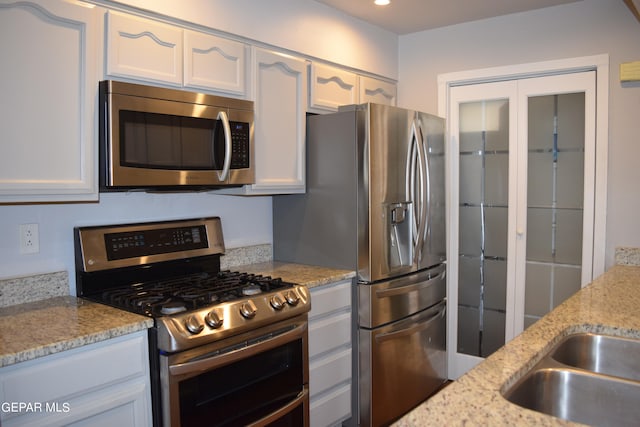 kitchen featuring white cabinetry, appliances with stainless steel finishes, light stone counters, and sink