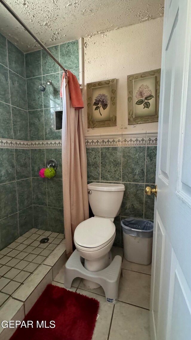 bathroom with tile walls, tile patterned floors, toilet, and curtained shower