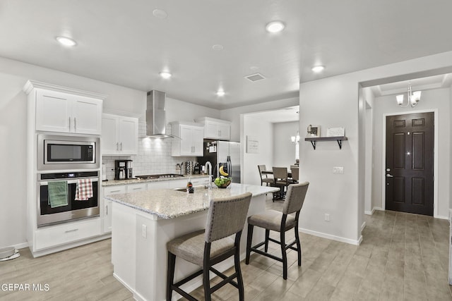 kitchen featuring wall chimney exhaust hood, white cabinetry, stainless steel appliances, a kitchen breakfast bar, and light wood-type flooring