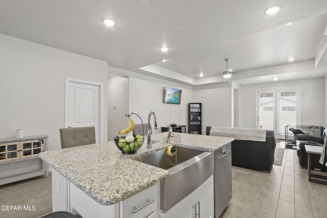 kitchen featuring light stone counters, sink, a kitchen island with sink, white cabinetry, and a tray ceiling