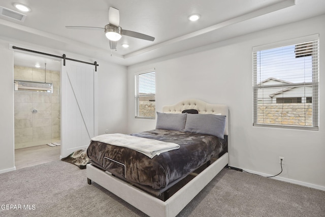 bedroom with a barn door, carpet flooring, a tray ceiling, ceiling fan, and ensuite bath