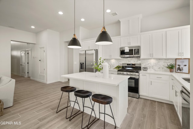 kitchen with appliances with stainless steel finishes, white cabinetry, a kitchen island, and light hardwood / wood-style flooring