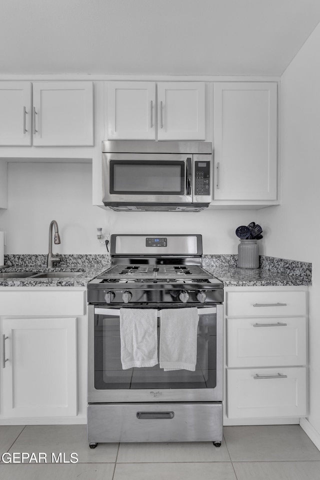 kitchen with stainless steel appliances, white cabinets, light tile patterned floors, and sink