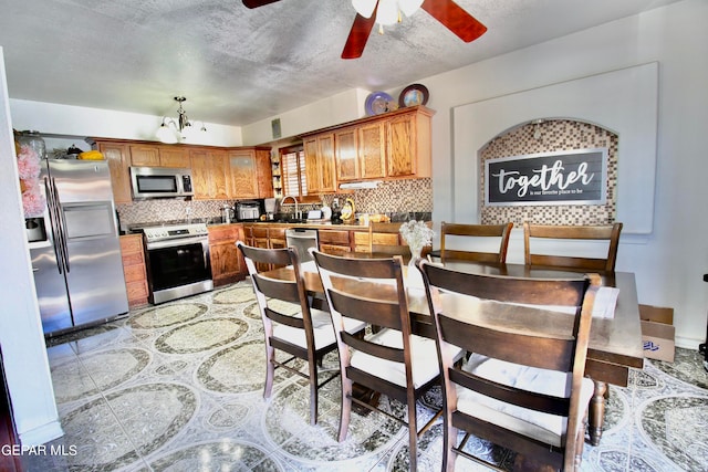 kitchen featuring stainless steel appliances, tasteful backsplash, sink, ceiling fan with notable chandelier, and a textured ceiling