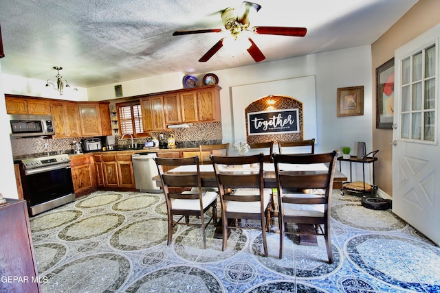 kitchen featuring sink, a textured ceiling, backsplash, appliances with stainless steel finishes, and ceiling fan with notable chandelier