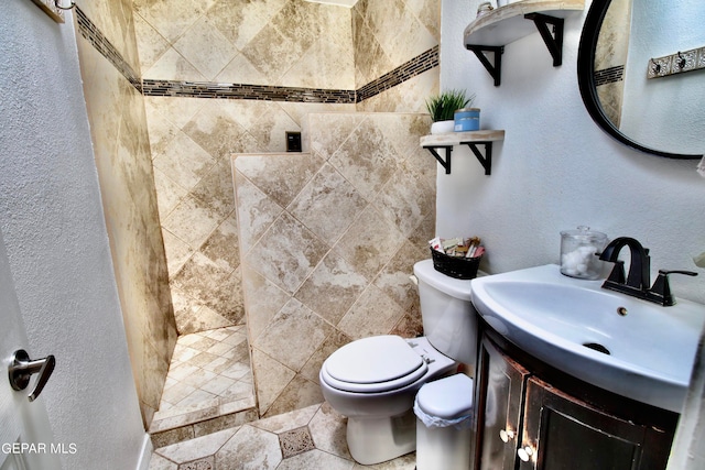 bathroom with a tile shower, vanity, and toilet