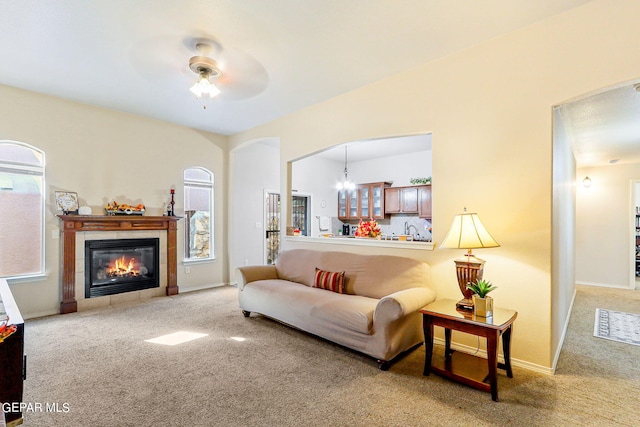 living room featuring ceiling fan with notable chandelier, carpet flooring, and a fireplace