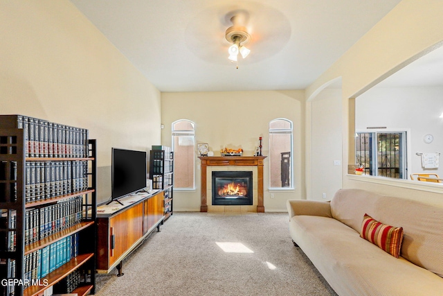 living room featuring a tiled fireplace, ceiling fan, and light colored carpet