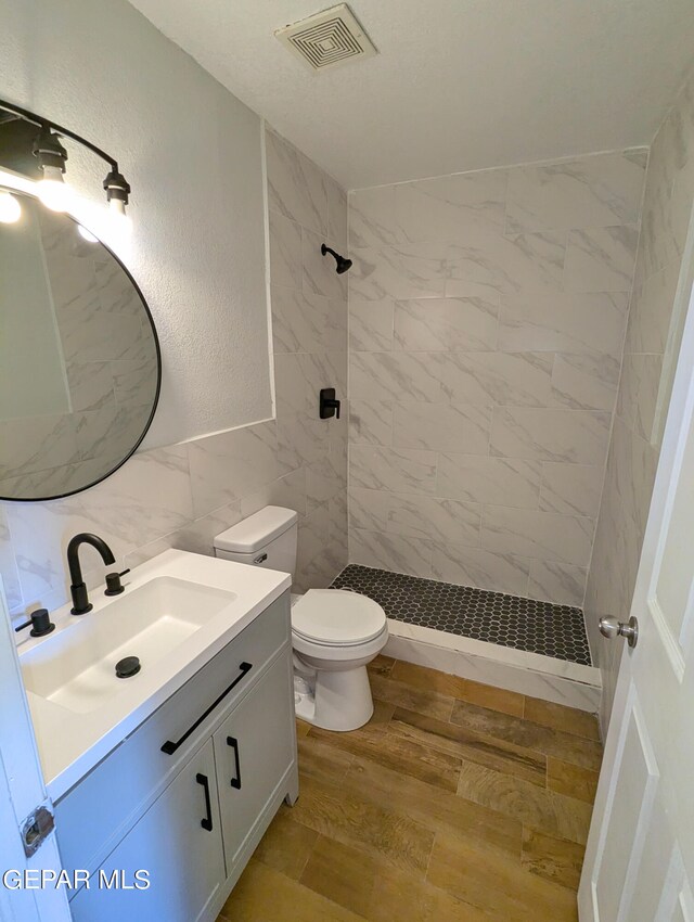 bathroom featuring tile walls, wood-type flooring, tiled shower, vanity, and toilet