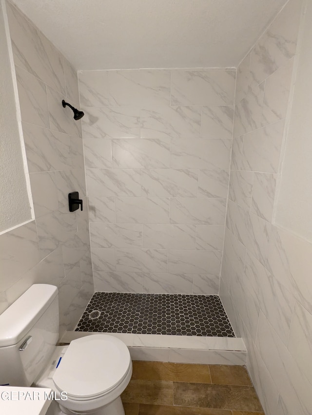 bathroom with toilet, tile walls, and a tile shower