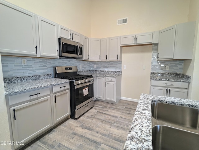 kitchen featuring light stone countertops, stainless steel appliances, a towering ceiling, and decorative backsplash