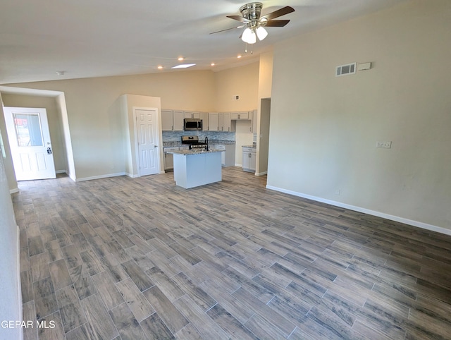 kitchen with ceiling fan, an island with sink, lofted ceiling, hardwood / wood-style flooring, and stainless steel appliances