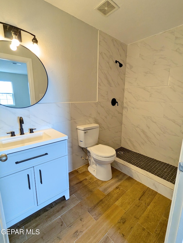 bathroom with vanity, tiled shower, wood-type flooring, tile walls, and toilet