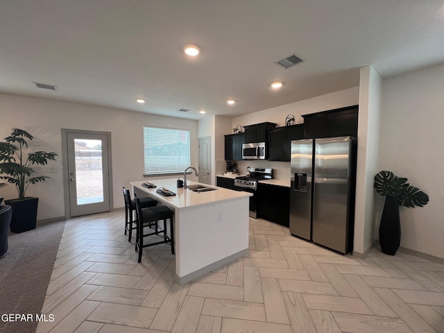 kitchen with appliances with stainless steel finishes, a breakfast bar area, light parquet floors, a center island with sink, and sink