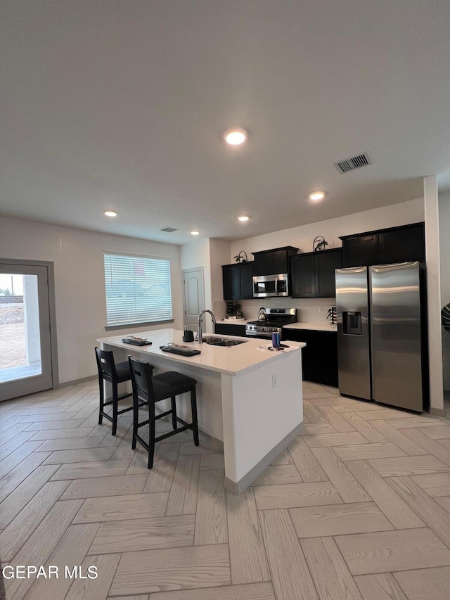 kitchen featuring sink, light parquet flooring, a center island with sink, appliances with stainless steel finishes, and a breakfast bar area