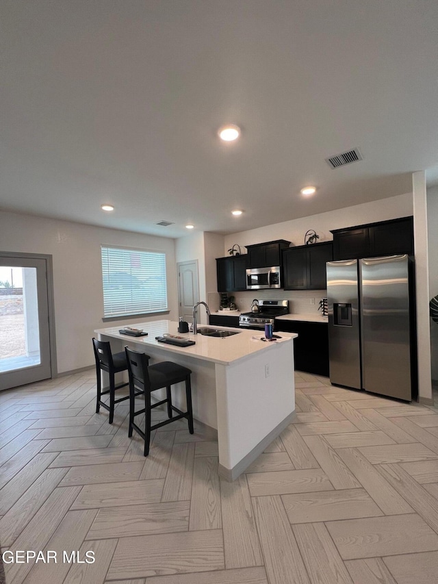 12832 Star Gaze Ave, El Paso, TX 79928 - kitchen with appliances with stainless steel finishes, dark cabinetry, a sink, a center island with sink, and light countertops