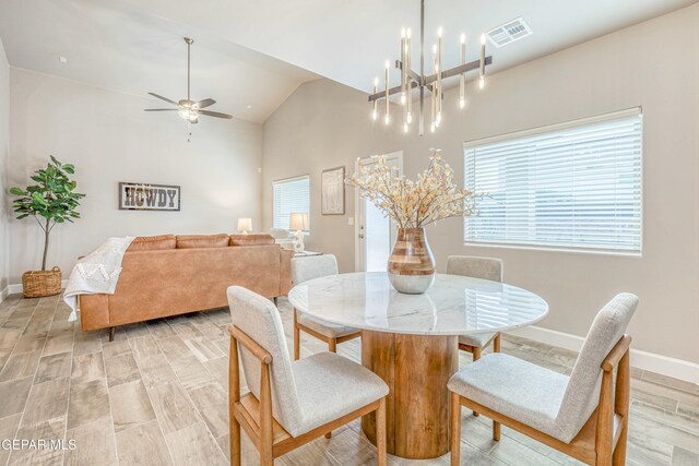 dining space featuring ceiling fan with notable chandelier, light wood-type flooring, and vaulted ceiling