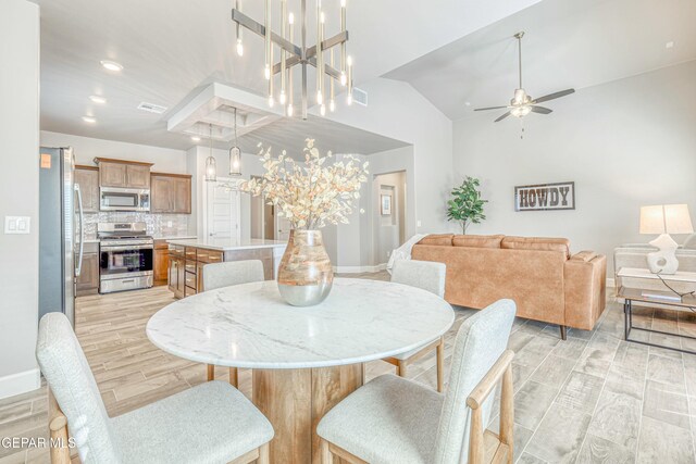 dining room with ceiling fan with notable chandelier, light hardwood / wood-style floors, and high vaulted ceiling