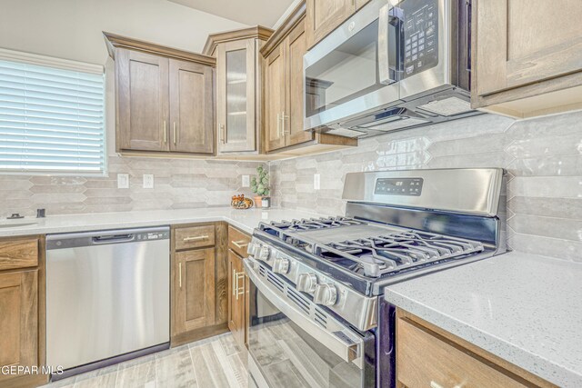 kitchen featuring appliances with stainless steel finishes, light wood-type flooring, tasteful backsplash, and light stone counters