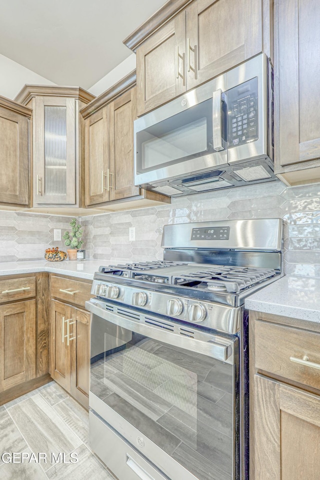 kitchen with decorative backsplash, light hardwood / wood-style flooring, stainless steel appliances, and light stone counters