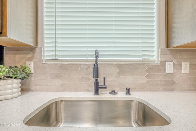 details featuring backsplash, light stone counters, and sink