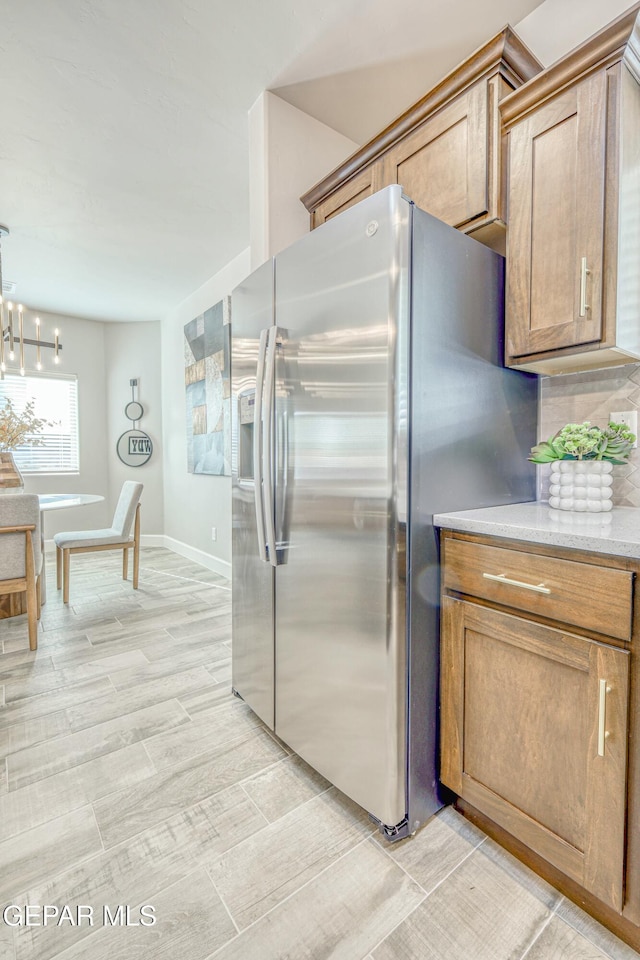 kitchen with stainless steel fridge with ice dispenser, backsplash, pendant lighting, a chandelier, and light wood-type flooring