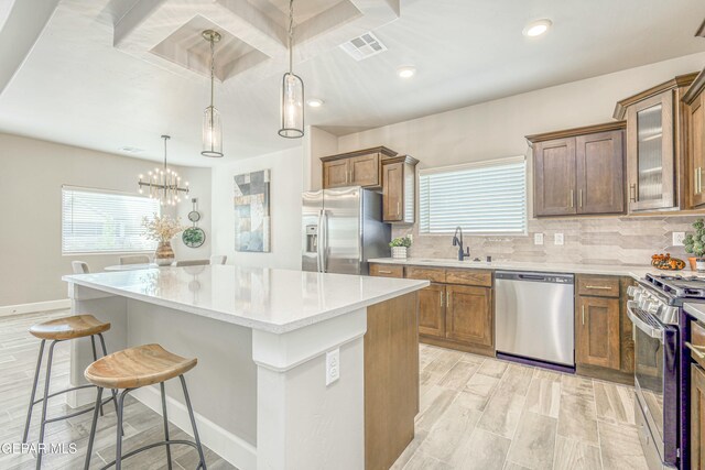 kitchen with sink, hanging light fixtures, appliances with stainless steel finishes, a kitchen island, and light wood-type flooring