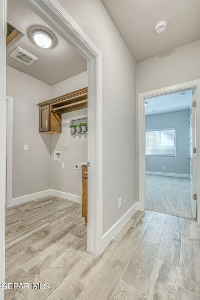 clothes washing area with hookup for an electric dryer, washer hookup, light hardwood / wood-style flooring, and cabinets