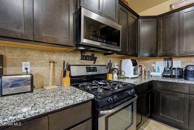 kitchen with dark brown cabinetry, light stone countertops, stainless steel appliances, and backsplash