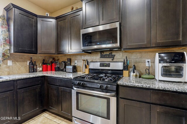 kitchen with dark brown cabinetry, light stone countertops, stainless steel appliances, and decorative backsplash