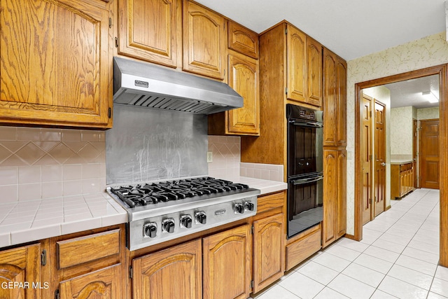 kitchen with light tile patterned flooring, stainless steel gas cooktop, decorative backsplash, exhaust hood, and double oven