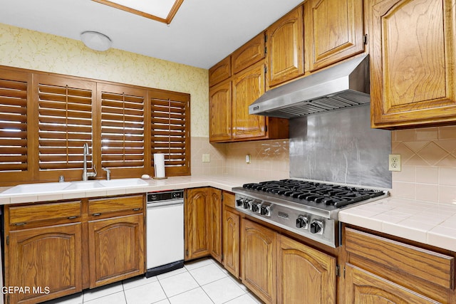 kitchen featuring light tile patterned flooring, sink, stainless steel gas cooktop, extractor fan, and tile counters